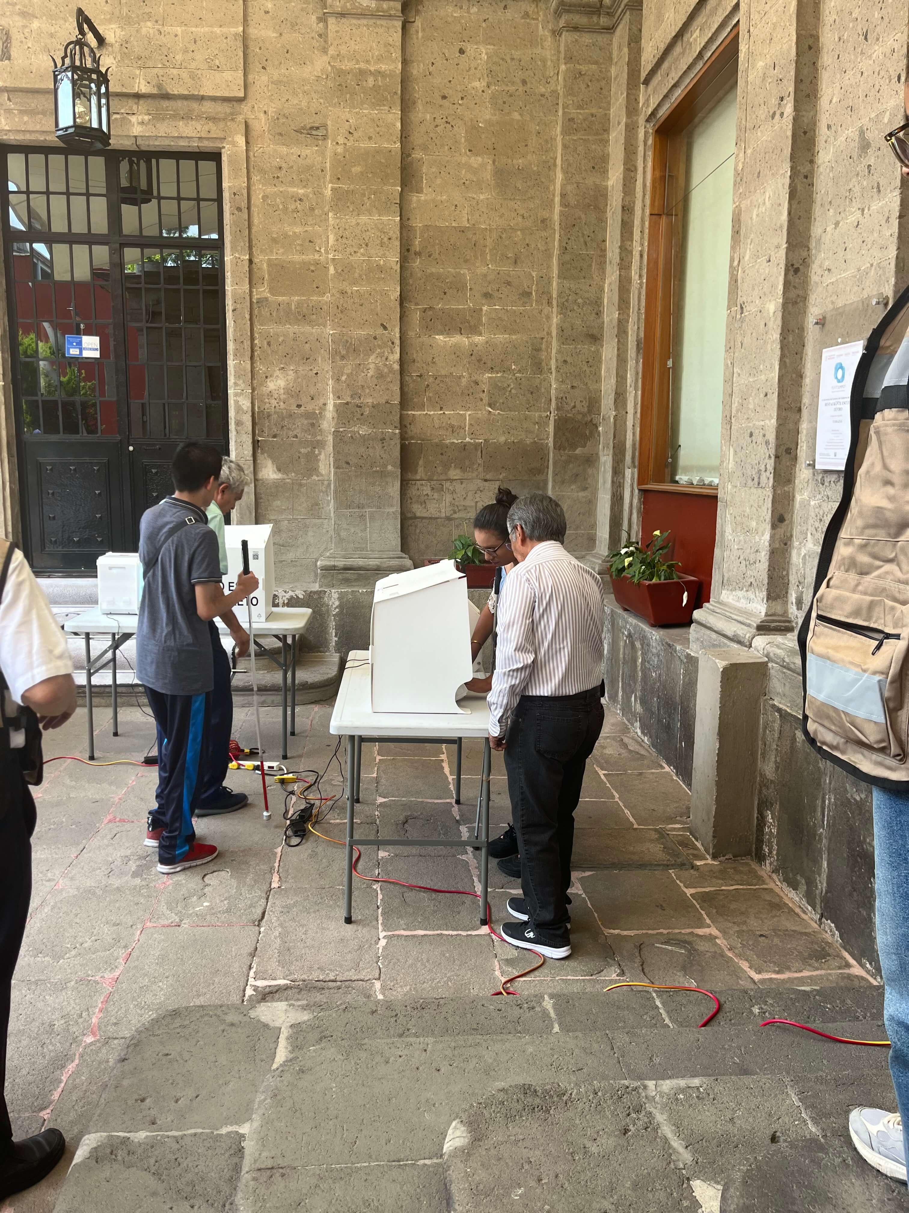Au Mexique, un membre du personnel électoral aide une personne avec des limitations visuelles à voter à l’aide de l’urne électronique du vote spécial (conçu pour les personnes hors circonscription).