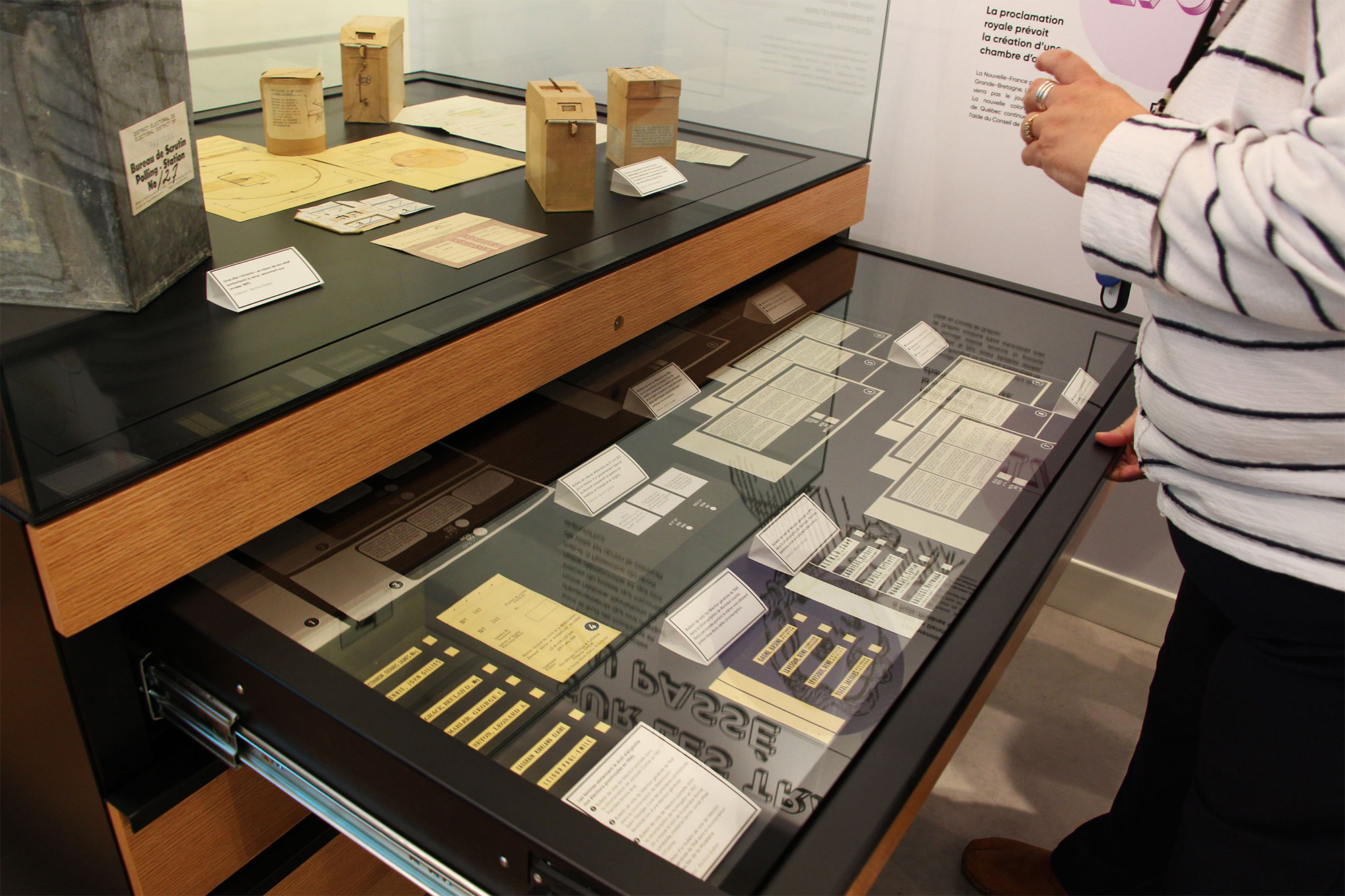 Vitrine d’objets historiques, une personne en chandail rayé observe attentivement.