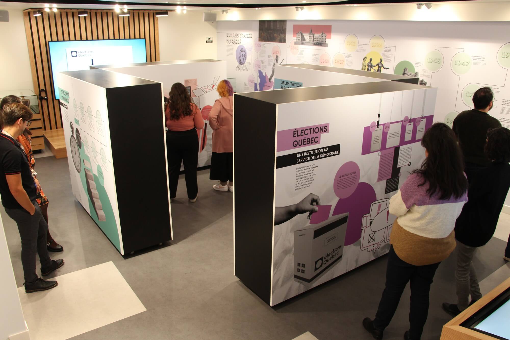 Des personnes dans une salle d’exposition observent des panneaux informatifs sur les élections.