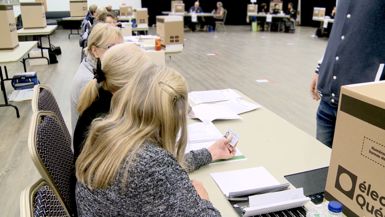 Plan rapproché de membres du personnel qui vérifient l’identité d’un électeur. L’une des femmes tend le permis de conduire de l’électeur à sa collègue.